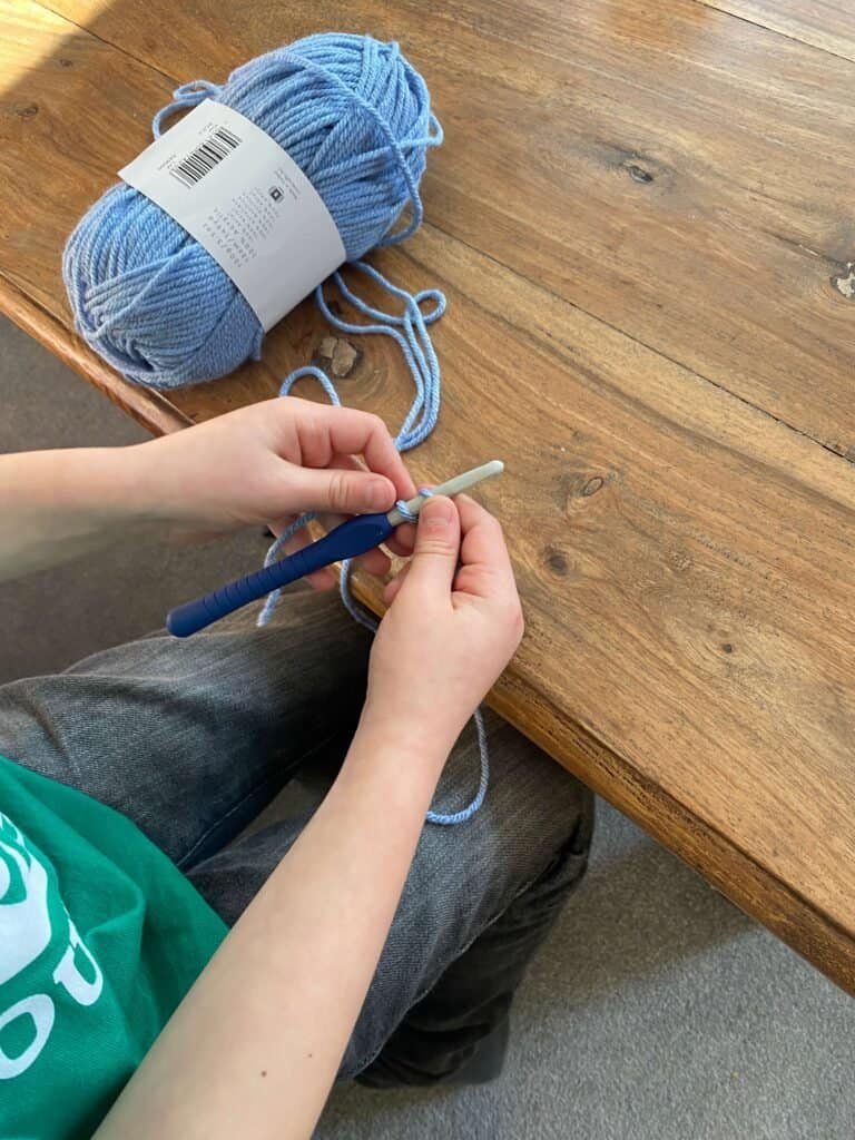 A child is crocheting with a hook and yarn