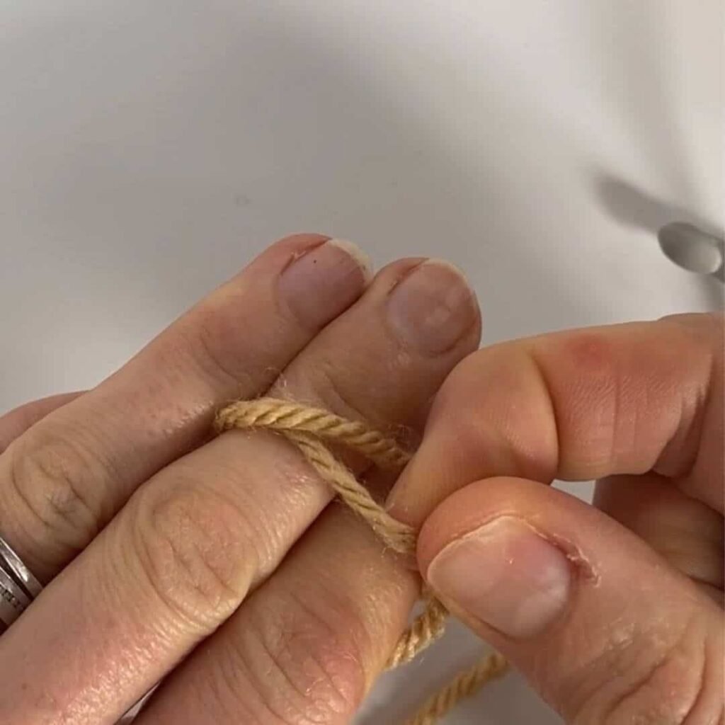 image showing yarn wrapped twice around 2 fingers, and one loop being pulled over the other again