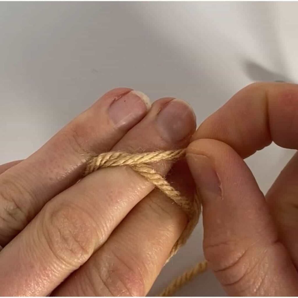 image showing yarn wrapped twice around 2 fingers, and one loop being pulled over the other