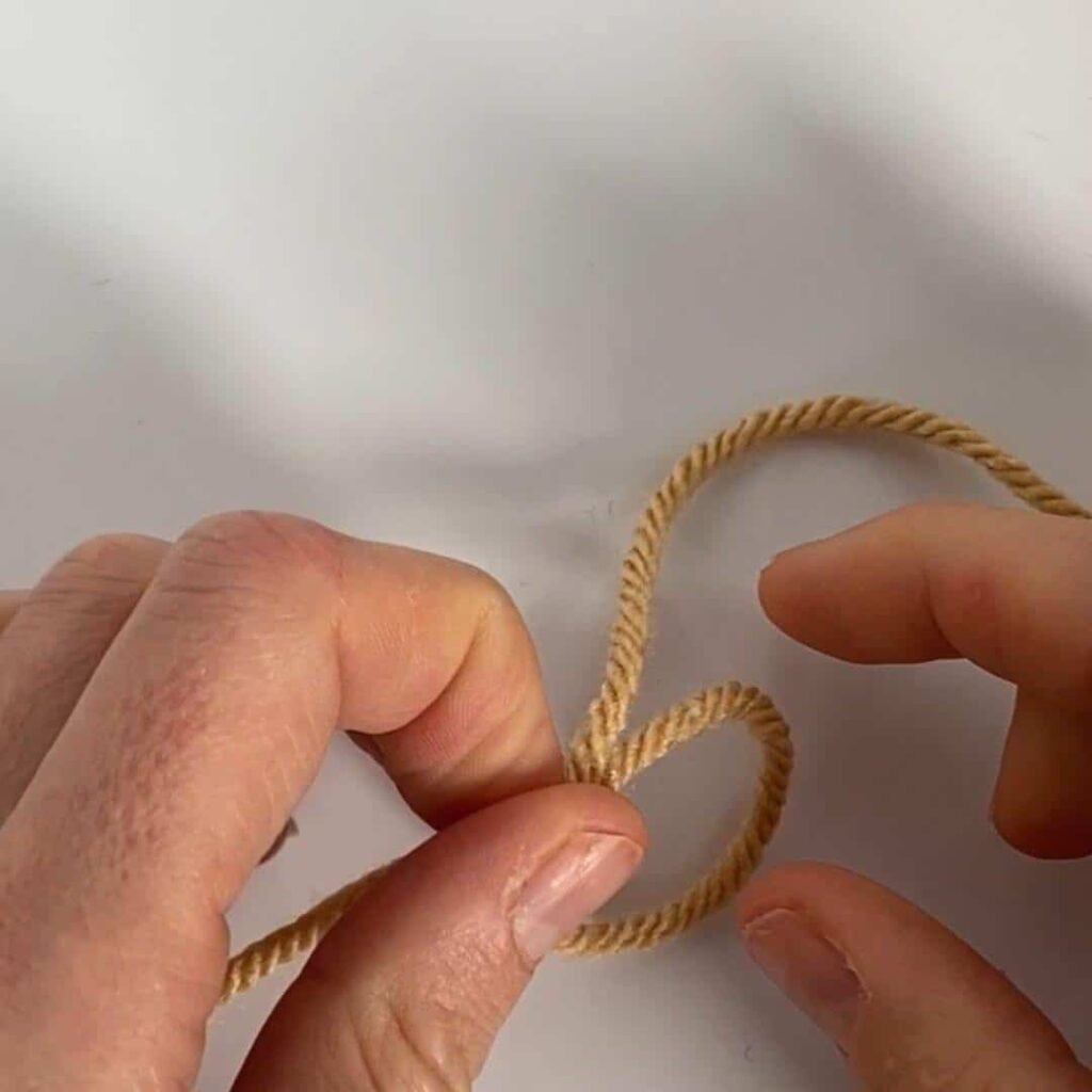 Hands picking up a loop of yarn to make a slipknot