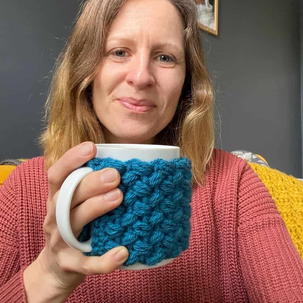 warm hands crochet mug cosy being held by designer