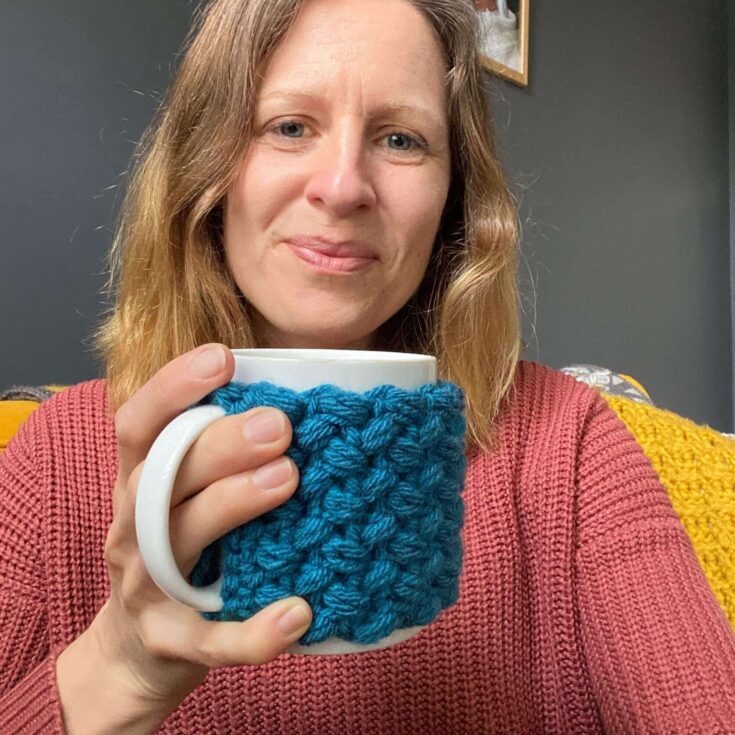 Owner of Concrete Gems holding a mug with a mug cosy on