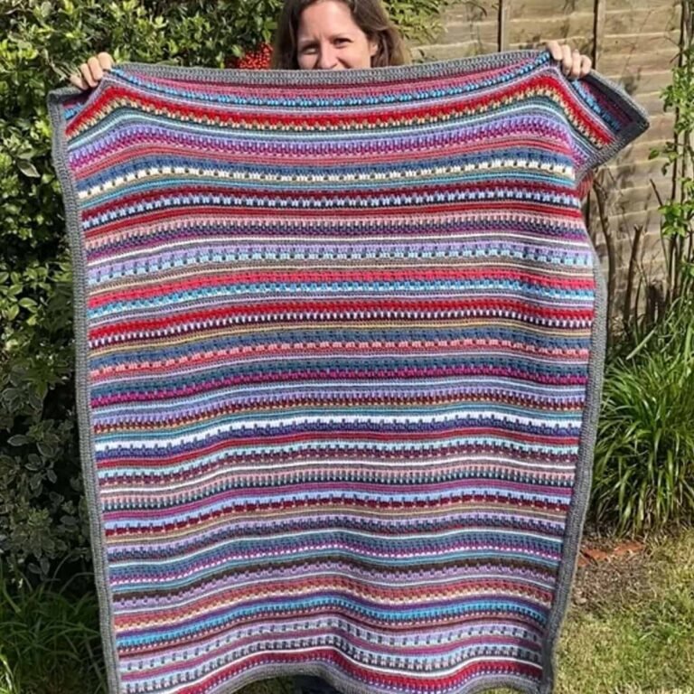 designer holding up the reversible rainbow crochet blanket in the garden