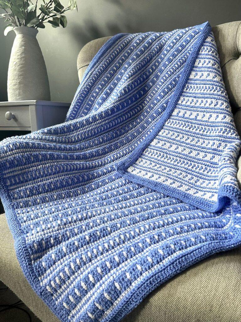 A blue and white mosaic crochet blanket laid on a sofa showing that it is 2 sided