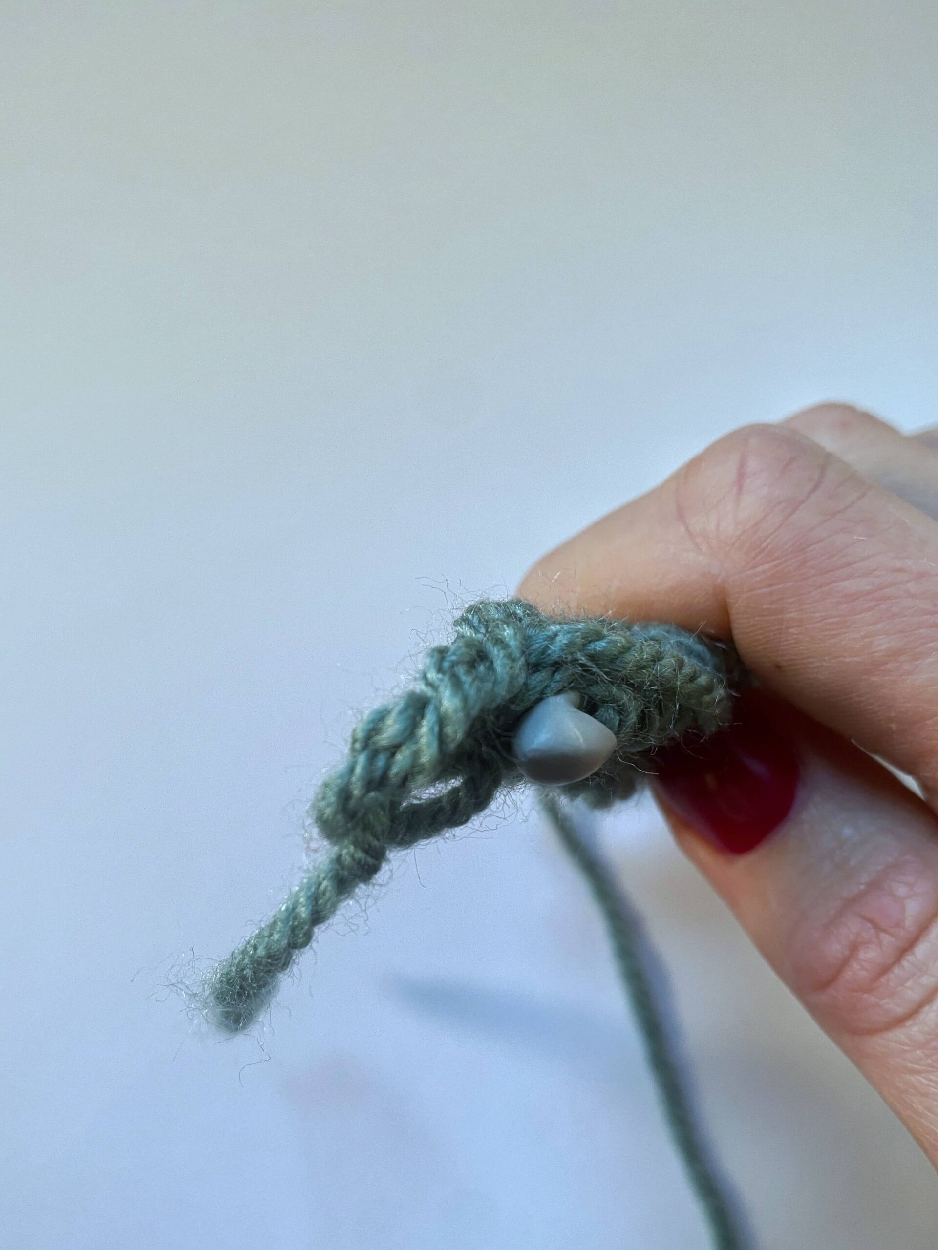 A hand holding a crocheted fabric end on, showing where to insert the hook for the last stitch