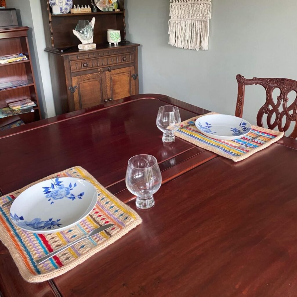 A wooden table with crochet placemats, plates and wine glasses
