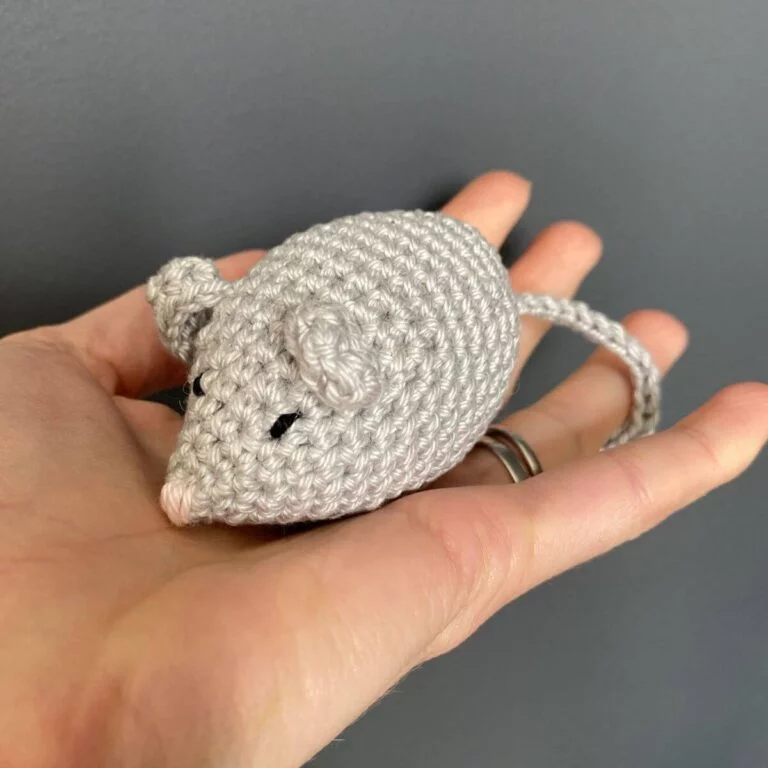 A crocheted grey mouse being held in a hand