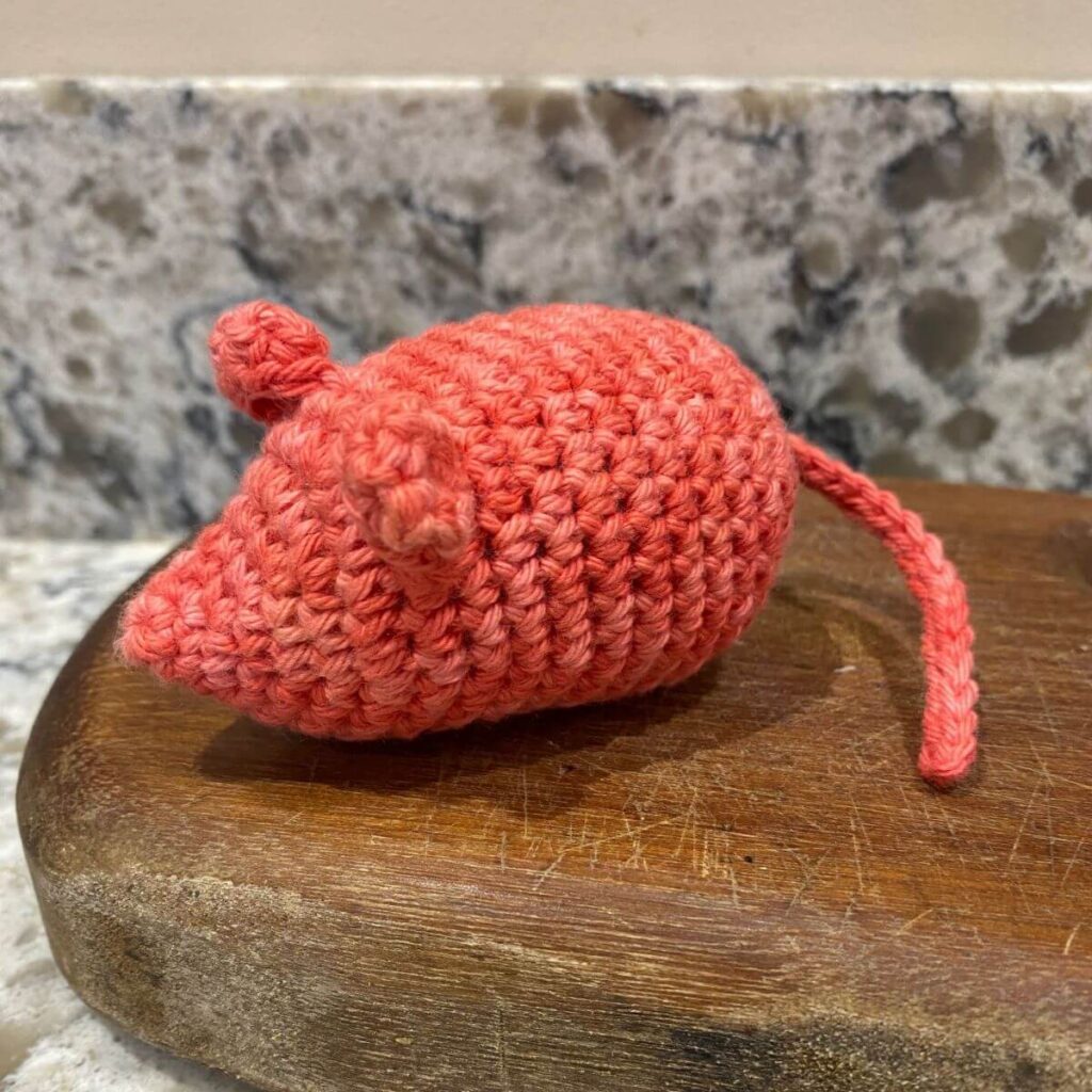 A pink crocheted mouse sat on a wooden board