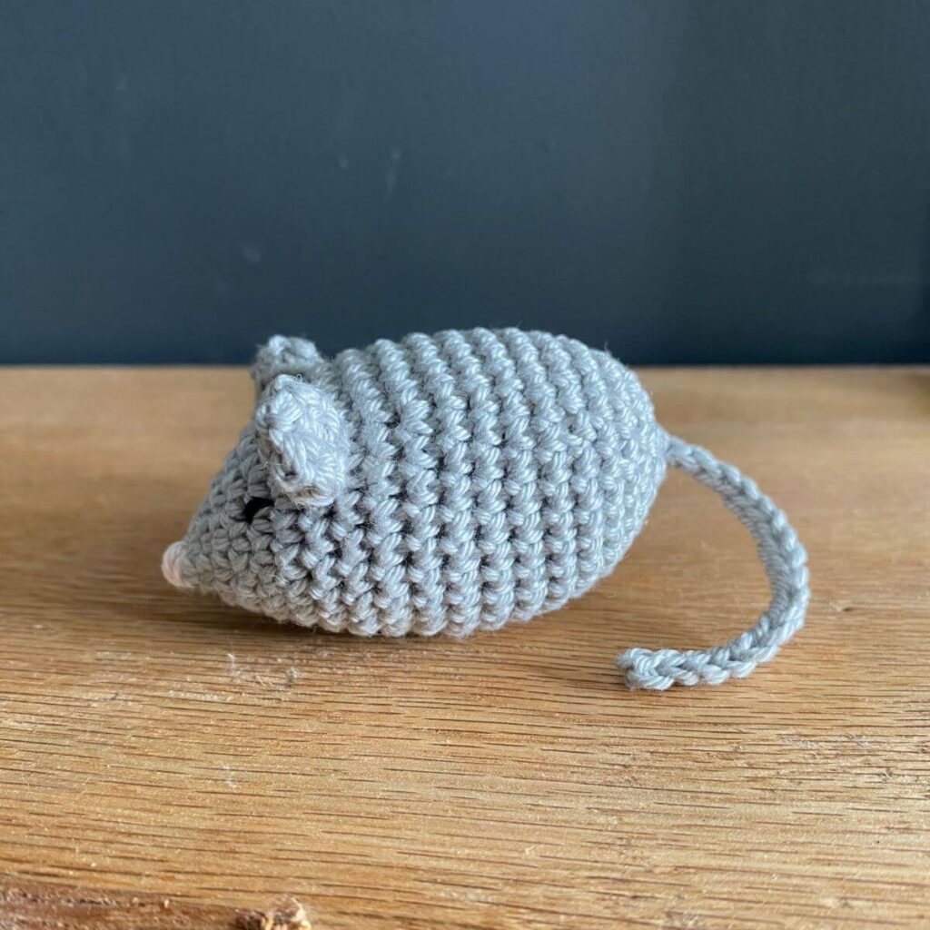 A cute crocheted mouse on a wooden shelf, crocheted using the munchkin mouse crochet pattern