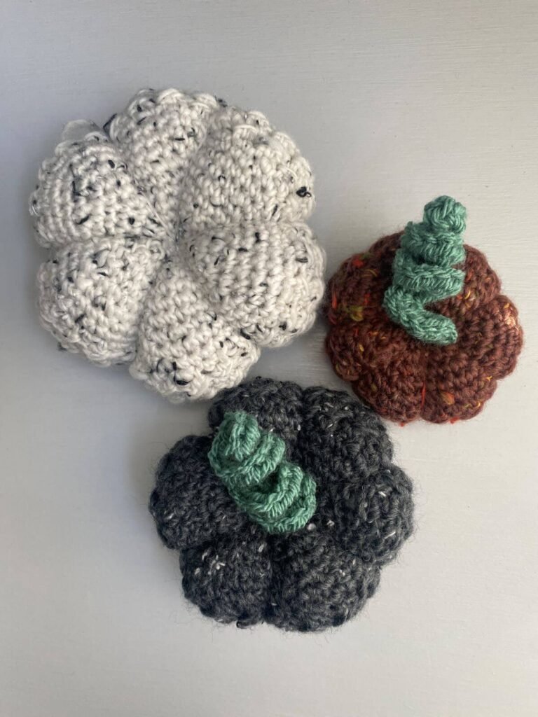 3 crocheted pumpkins in red, grey and white tweed. 2 have curly stems