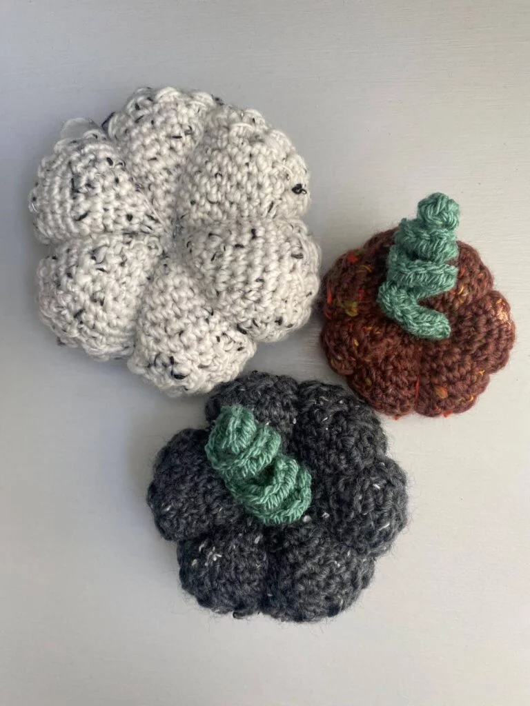 3 crocheted pumpkins in red, grey and white tweed. 2 have curly stems