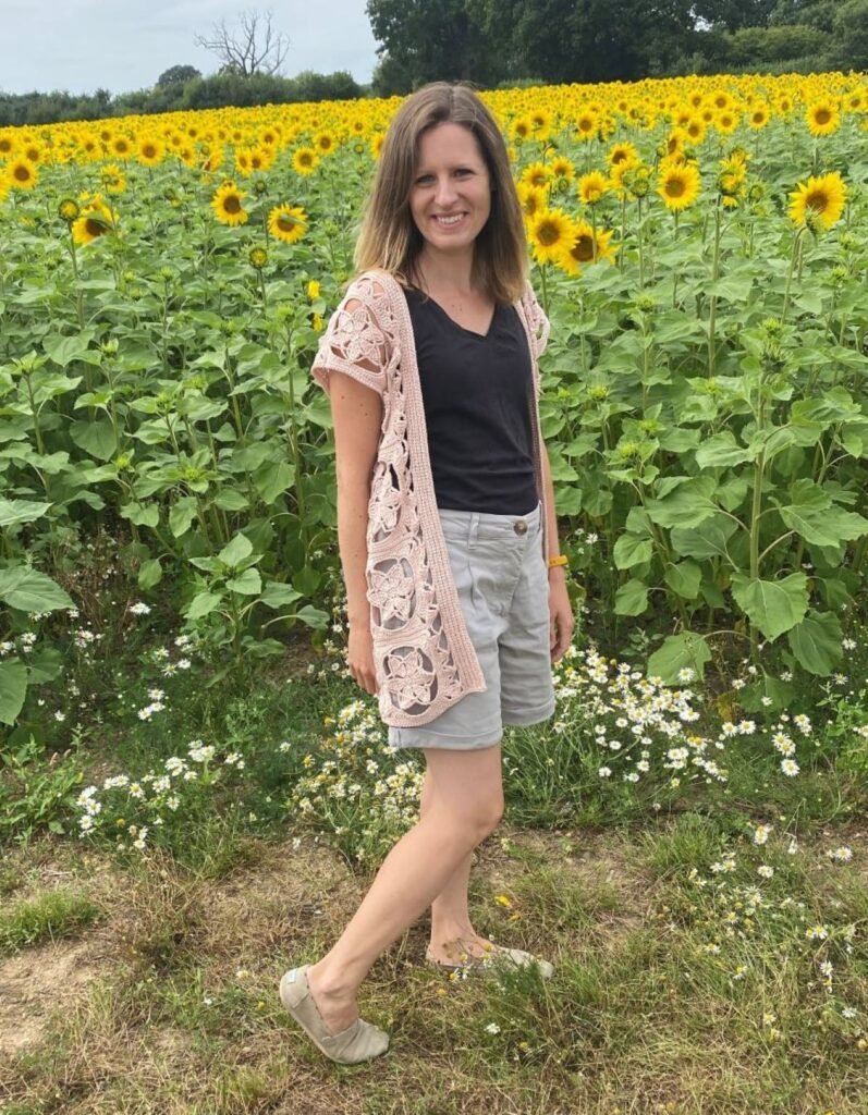 A lady wearing shorts, a tshirt and a crocheted cardigan in a field of sunflowers