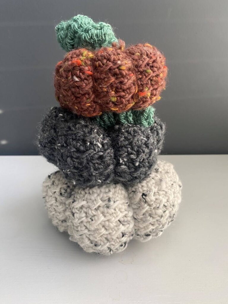 A stack of 3 different sized crocheted pumpkins in orange, grey and white tweed yarn