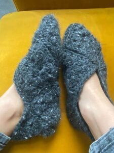 a pair of grey tweed crochet slippers are worn on 2 feet against a bright yellow fabric background