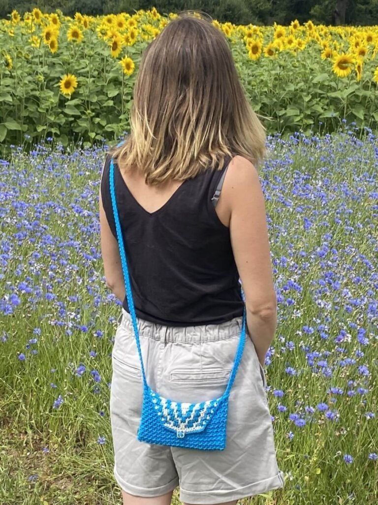 A lady wearing shorts and a vest looking over a field of sunflowers and wearing a cross body crochet bag in blue and cream