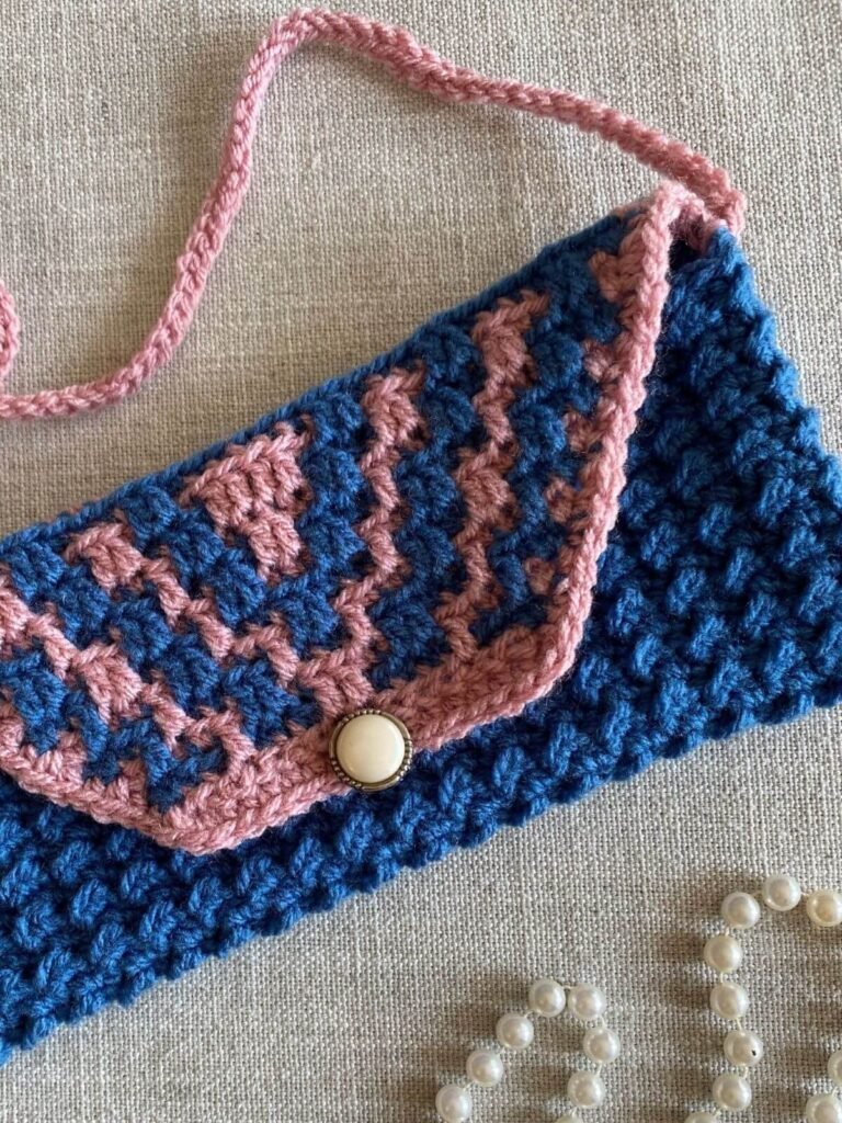 A vintage style crochet handbag in blue and pink with art deco patterning and a pink strap