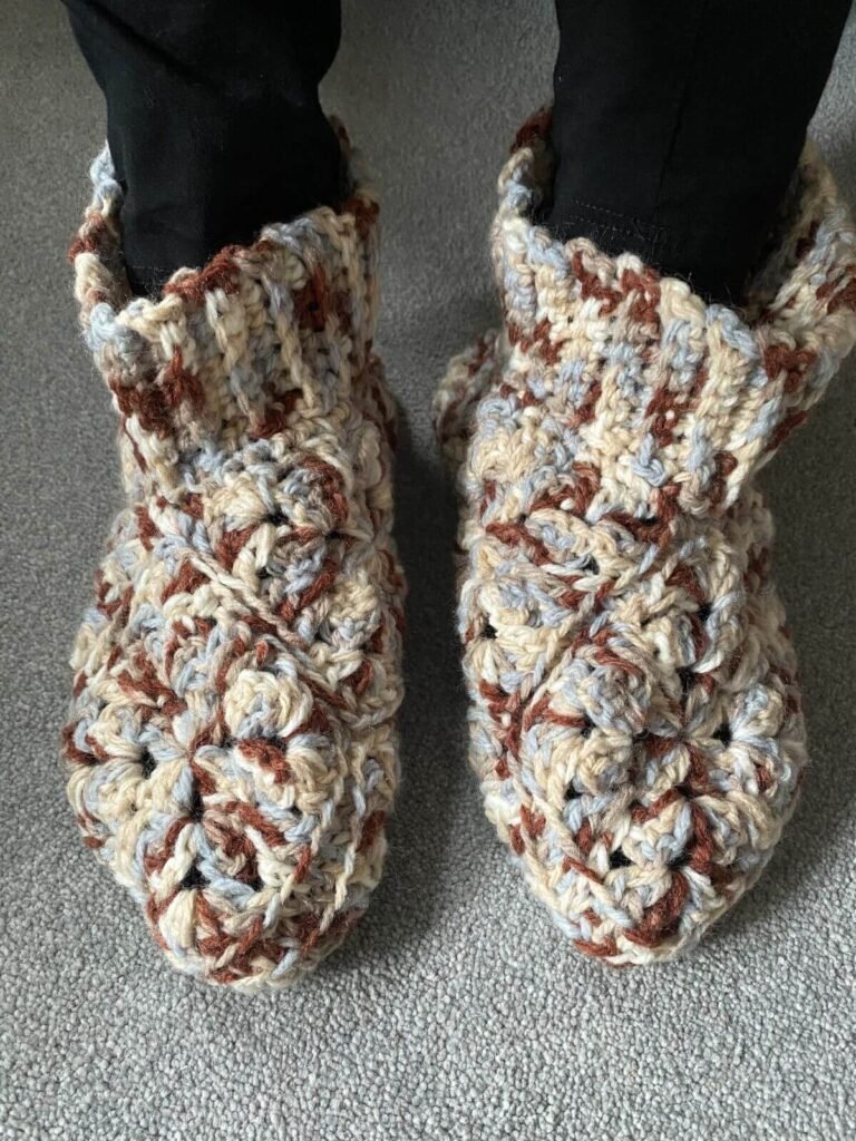 rustic crochet slipper boots in variegated brown and blue yarn is worn and stand on a grey carpet