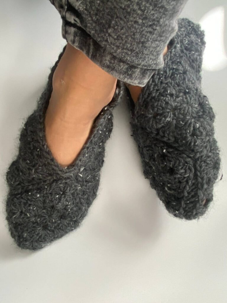 Crossed feet wearing jeans and crochet grey slippers