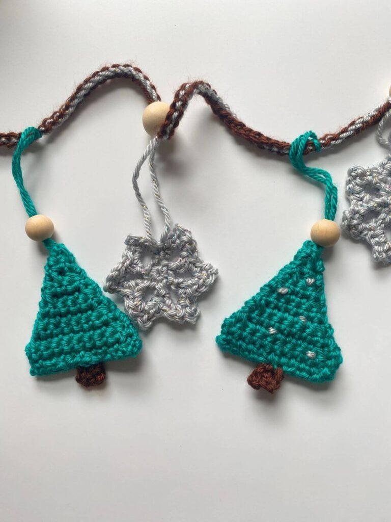 crochet green trees and silver snowflakes hang on a garland with wooden beads