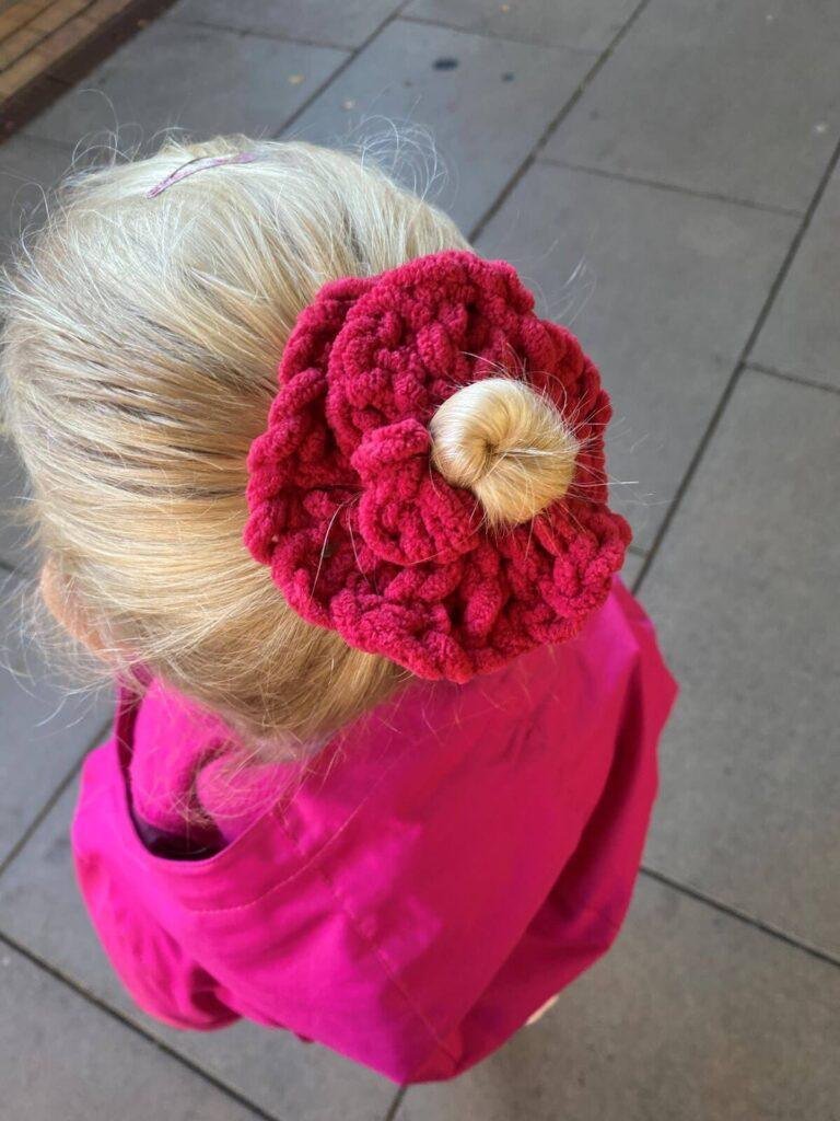 A girl with her back to the camera is wearing a pink top and has her hair tied up in a bun with a pink crochet scrunchie