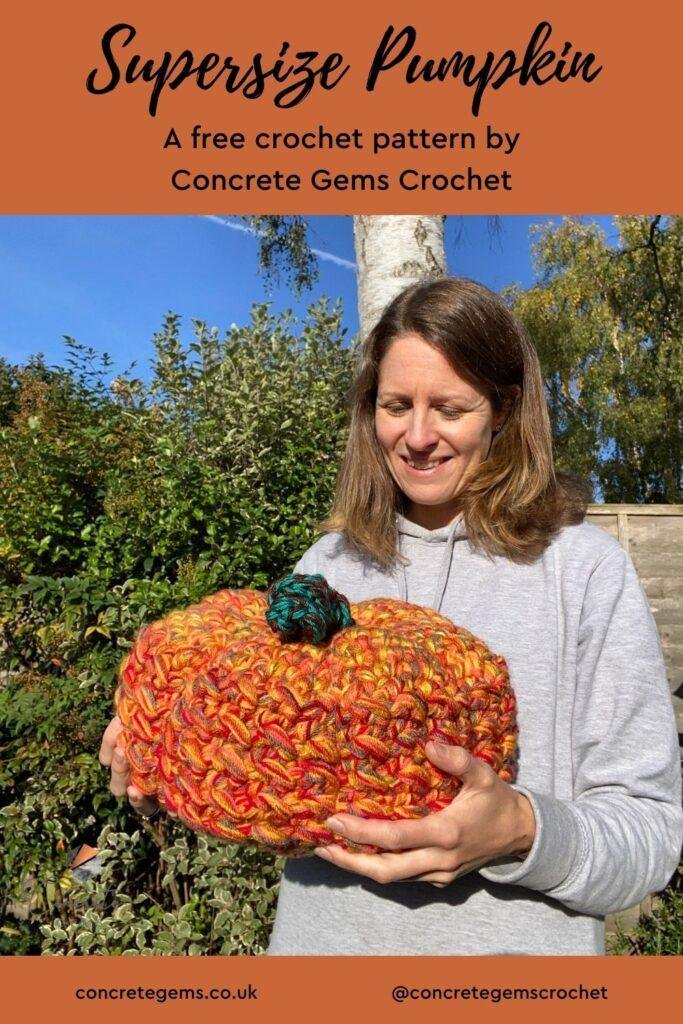 A lady holds a supersize crochet pumpkin in a garden