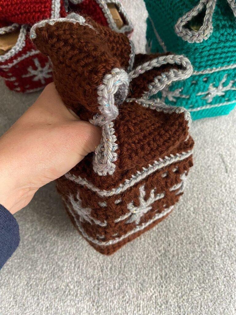A hand holding a crochet gift wrap at the top to make the bow