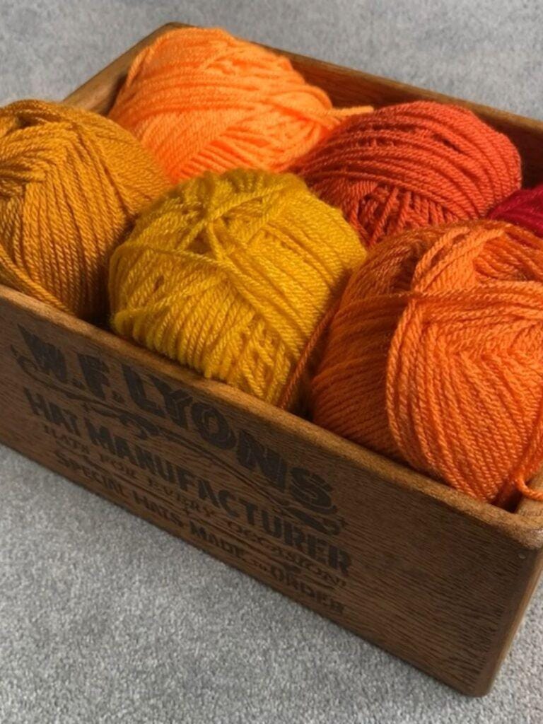 A wooden box of yellow and orange yarn