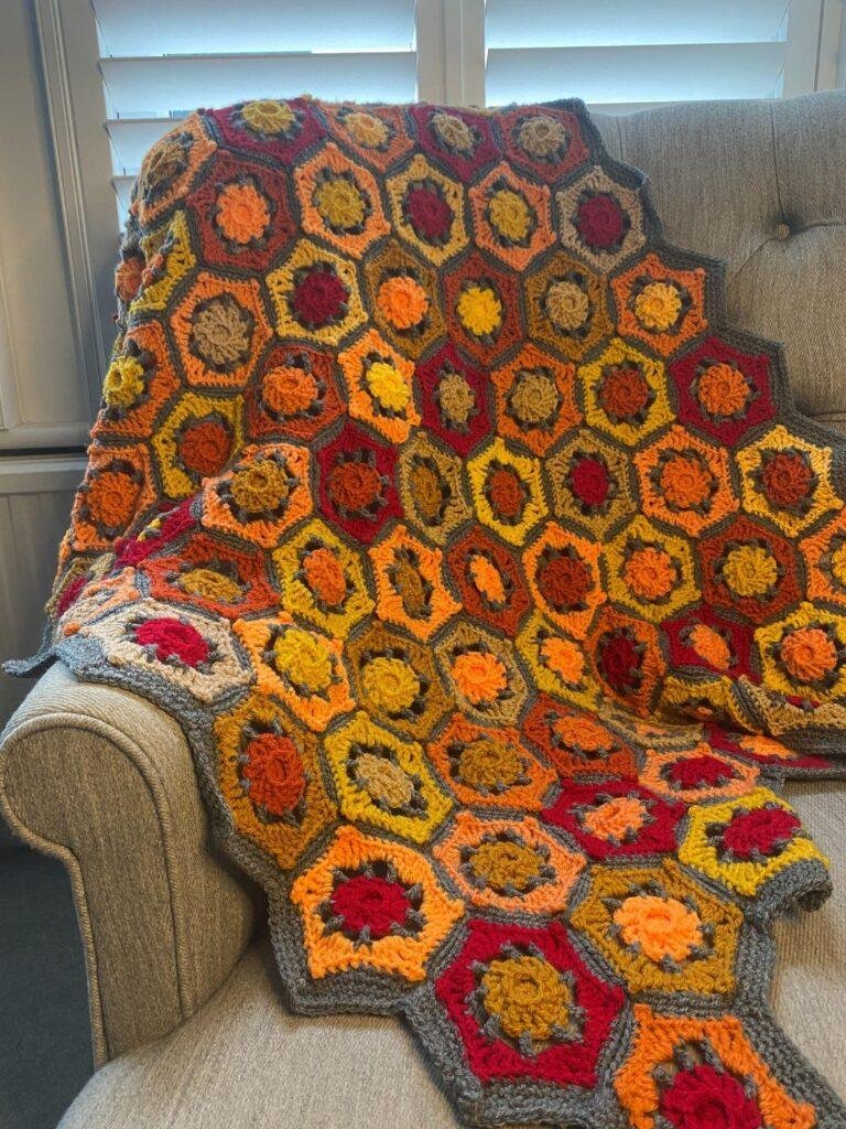 A red, orange and yellow, crochet hexagonal blanket is laid over the back of a chair
