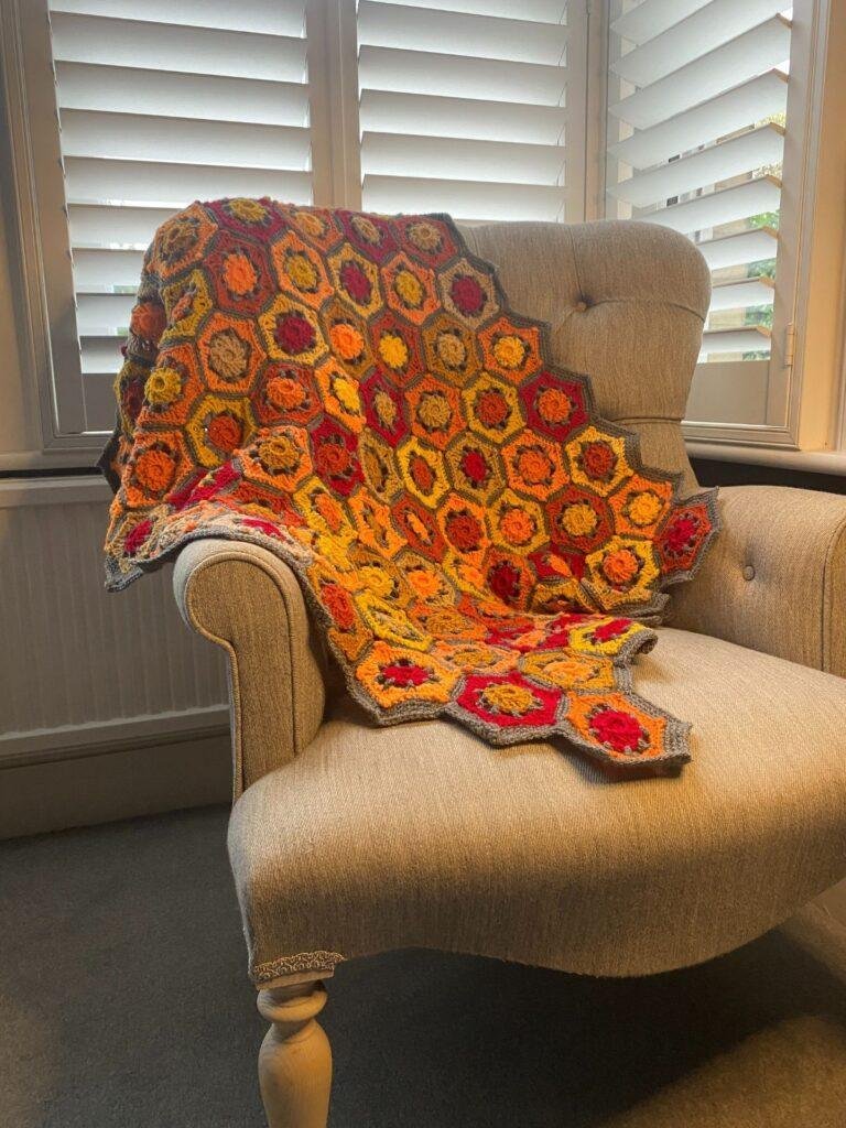 A yellow, orange and red crochet blanket is laid over an armchair