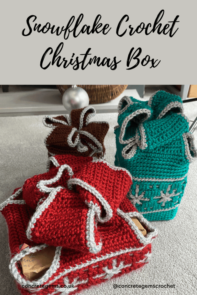 3 crochet gift boxes with silver snowflakes sit on the floor in red, green and brown