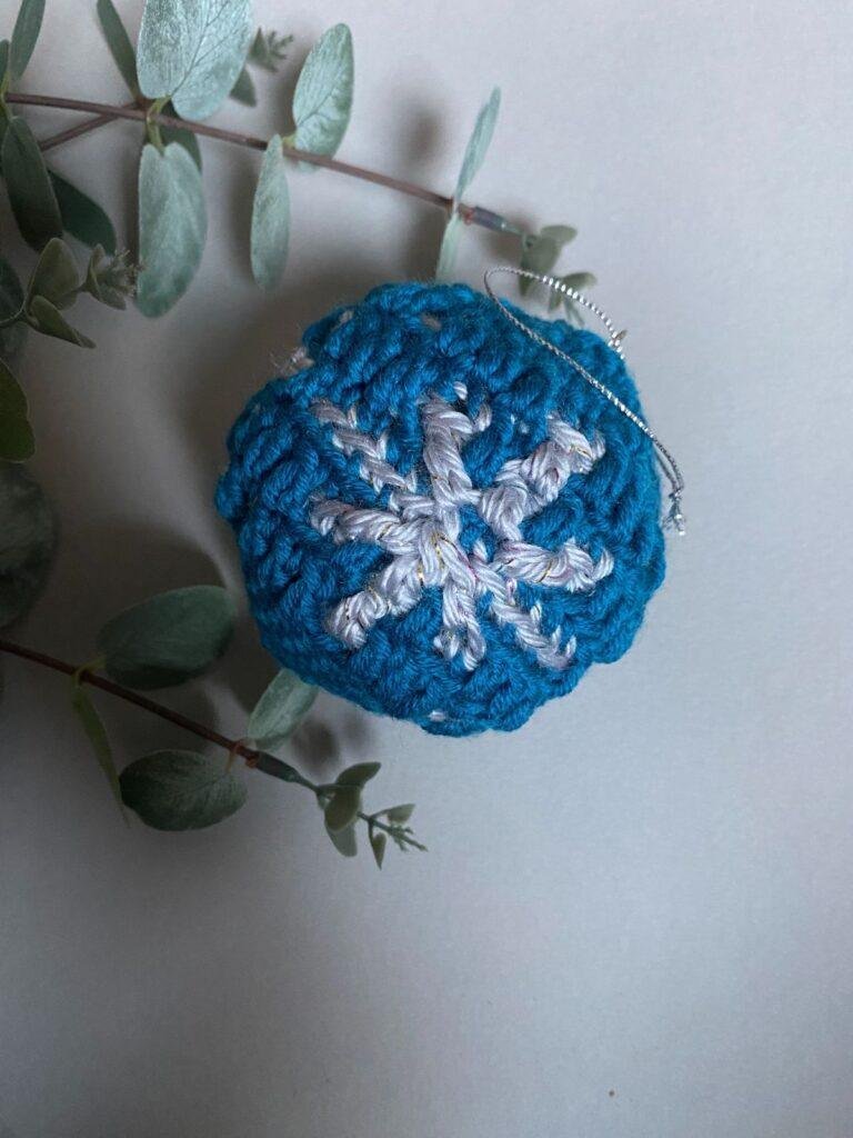 A blue crochet snowflake bauble sits amongst greenery