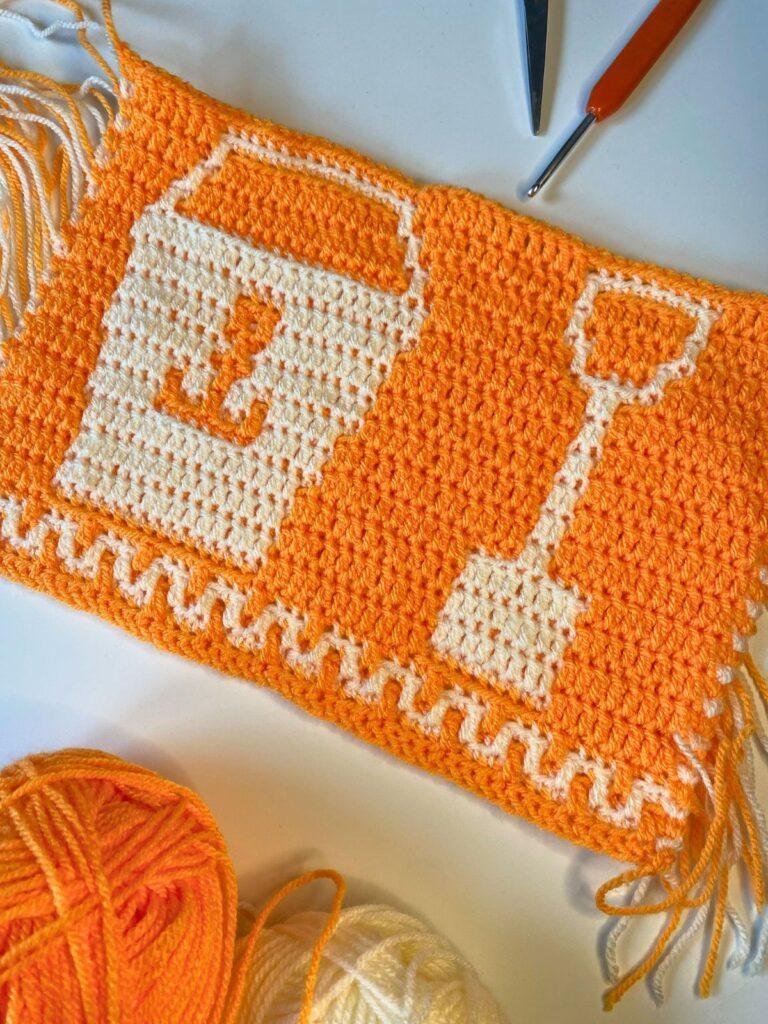 An orange and white crochet strip featuring bucket and spade motif