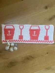 A strip of crochet in pink and white with buckets and spades on