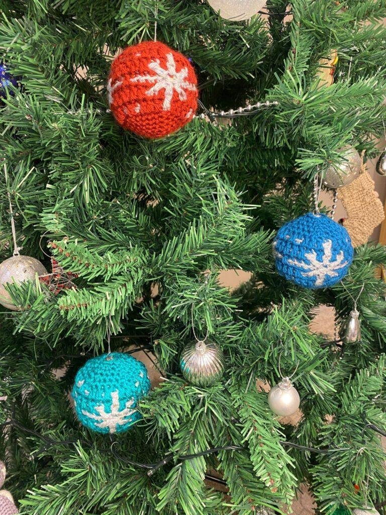 A red, green, and blue crochet bauble with Snowflake motif on, hang on a Christmas tree with other silver decorations