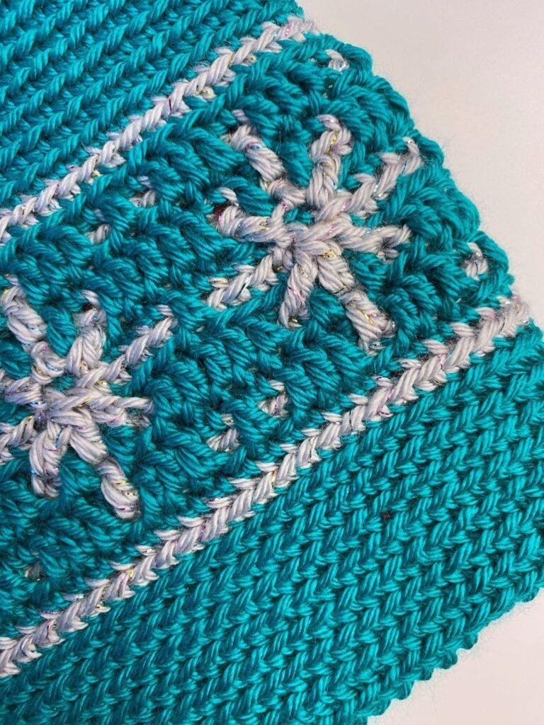 close up of a crochet book sleeve focussing on the silver snowflake motif on a green background