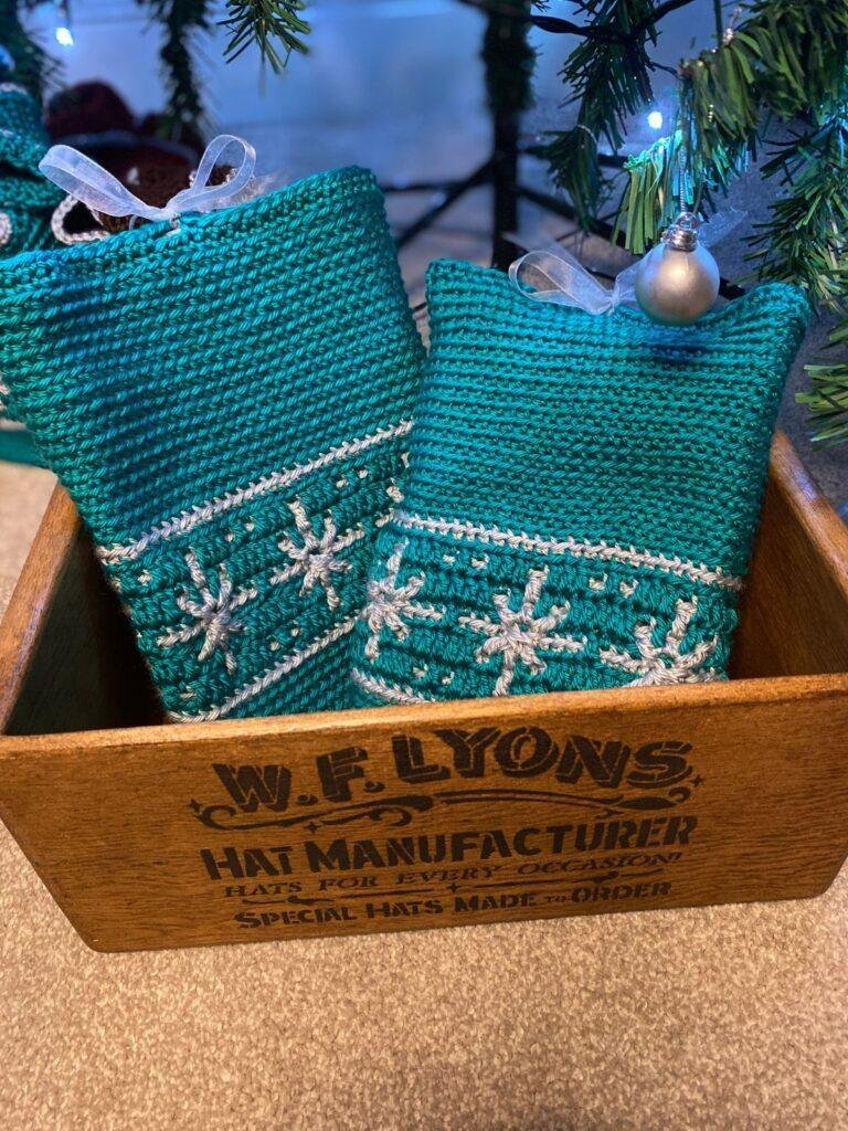 2 green crochet book covers with snowflakes on sit in a wooden box under a Christmas tree
