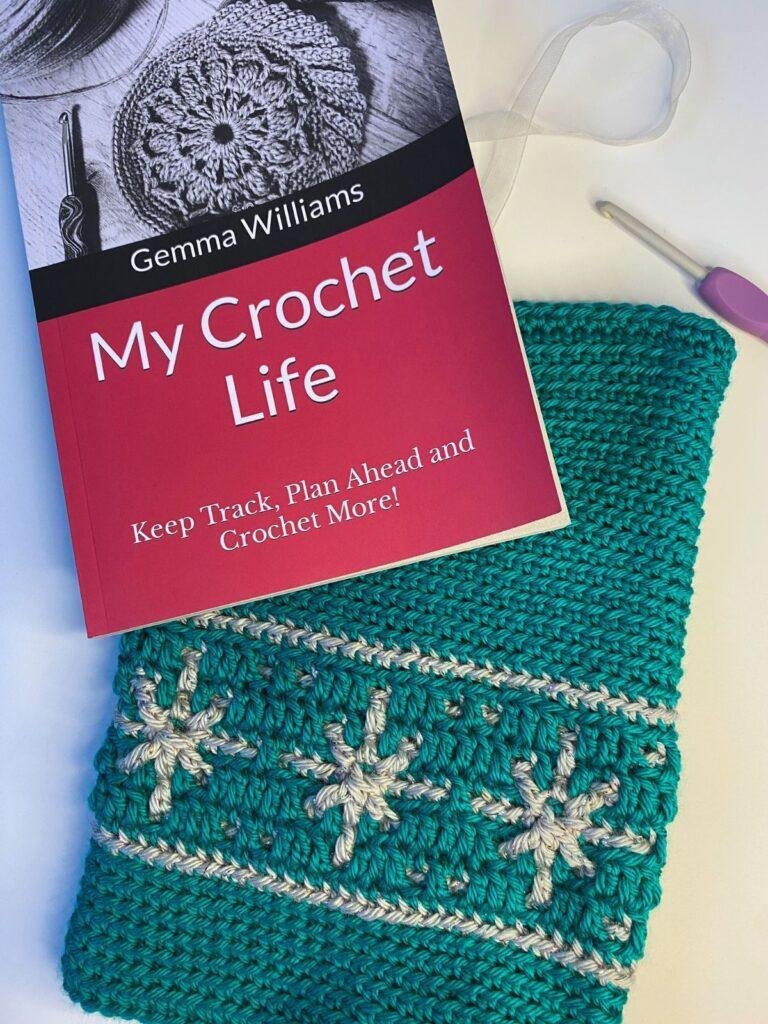 A green crochet book pouch lies under a journal called my crochet life