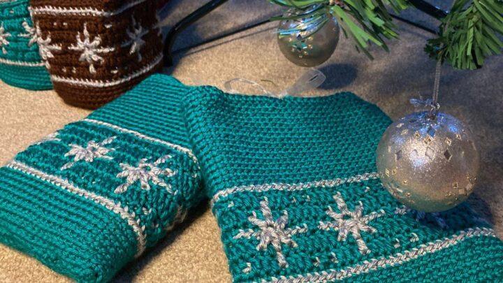 2 crochet book covers in green with snowflake motifs lay under a Christmas tree