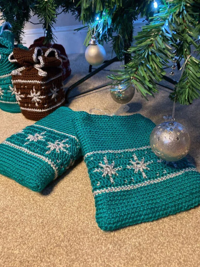 2 crochet book covers in green with snowflake motifs lay under a Christmas tree