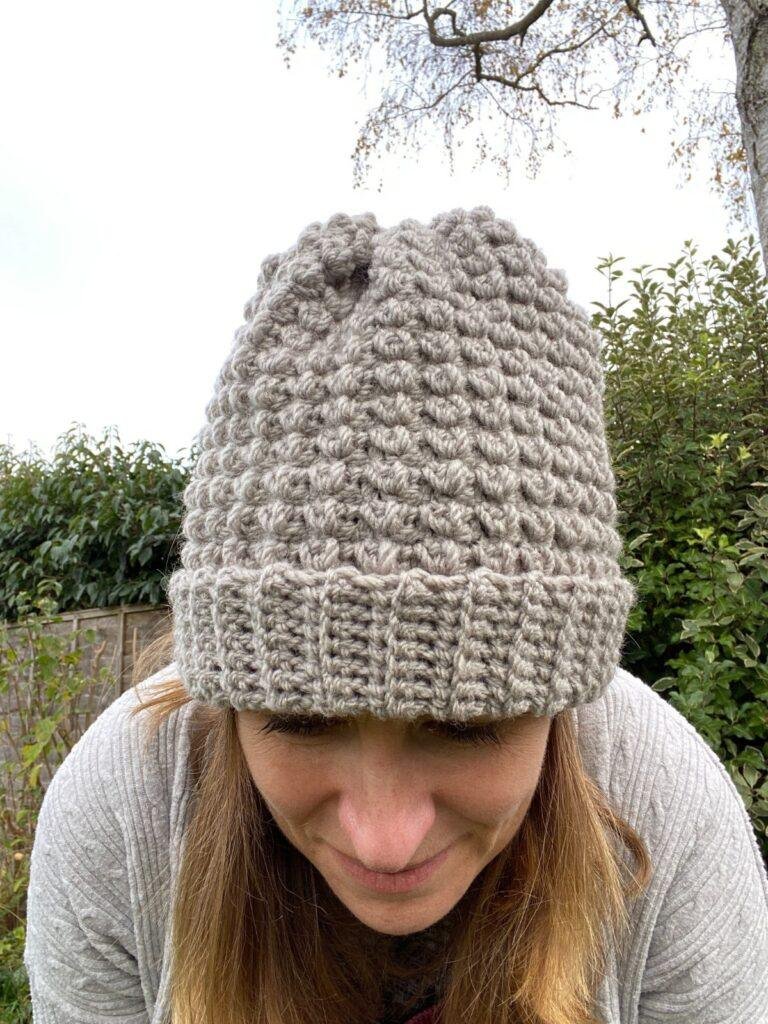 A lady bent forwards with her grey crochet hat in centre