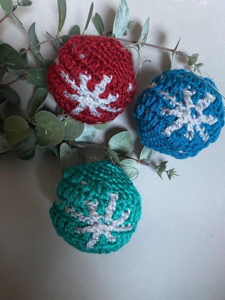 3 crochet baubles in red, green and blue with a snowflake motif in silver, all sitting on some eucalyptus