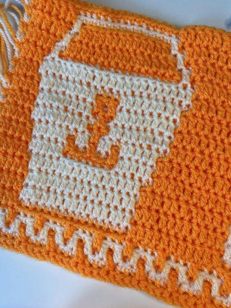 A seaside overlay mosaic crochet pattern of a bucket in cream on an orange background