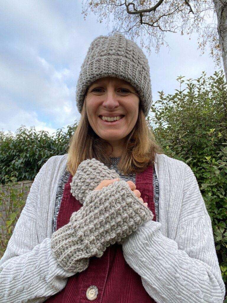 A lady wearing crochet grey hat and mittens in a garden