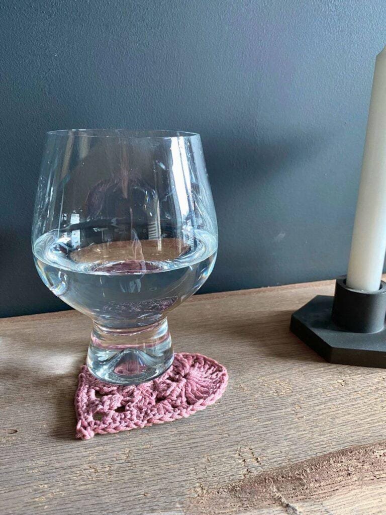 A pink heart coaster sits on a wooden shelf with a glass on top