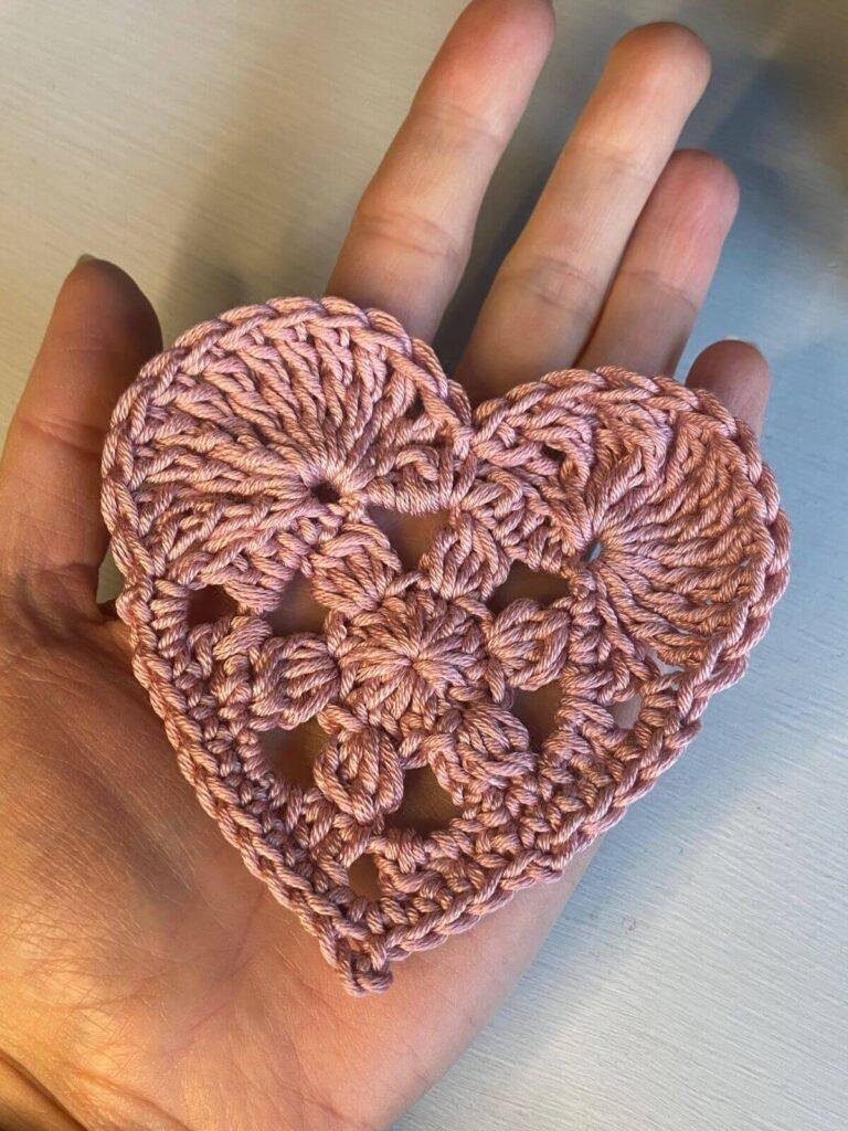 A hand holding a pink crocheted heart