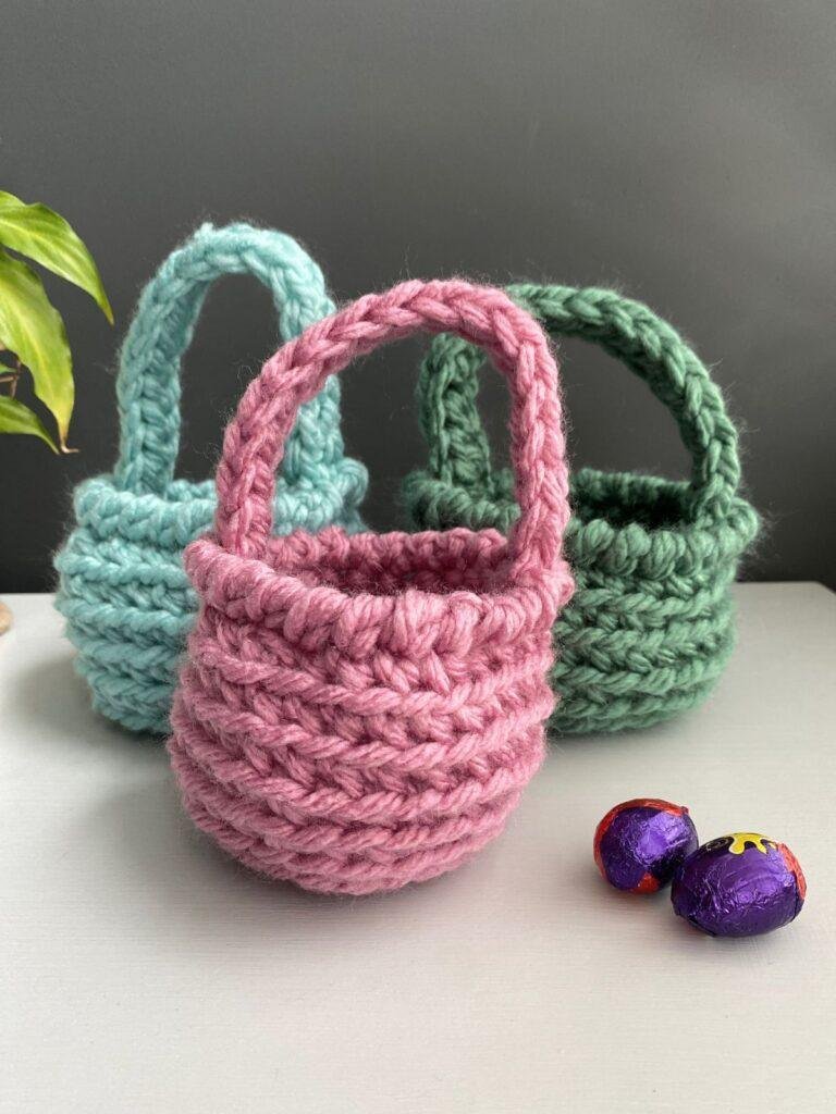 3 crochet woven baskets in green, blue and pink with mini chocolate eggs in the foreground