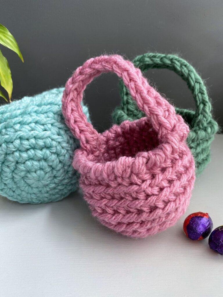3 crochet easter baskets in green, pink and blue. The blue one is lying down