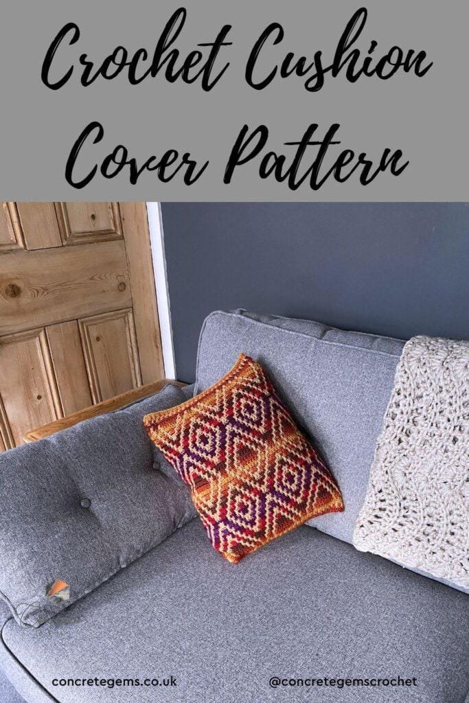 A geometric crochet cushion lays on a grey sofa next to a beige crochet blanket