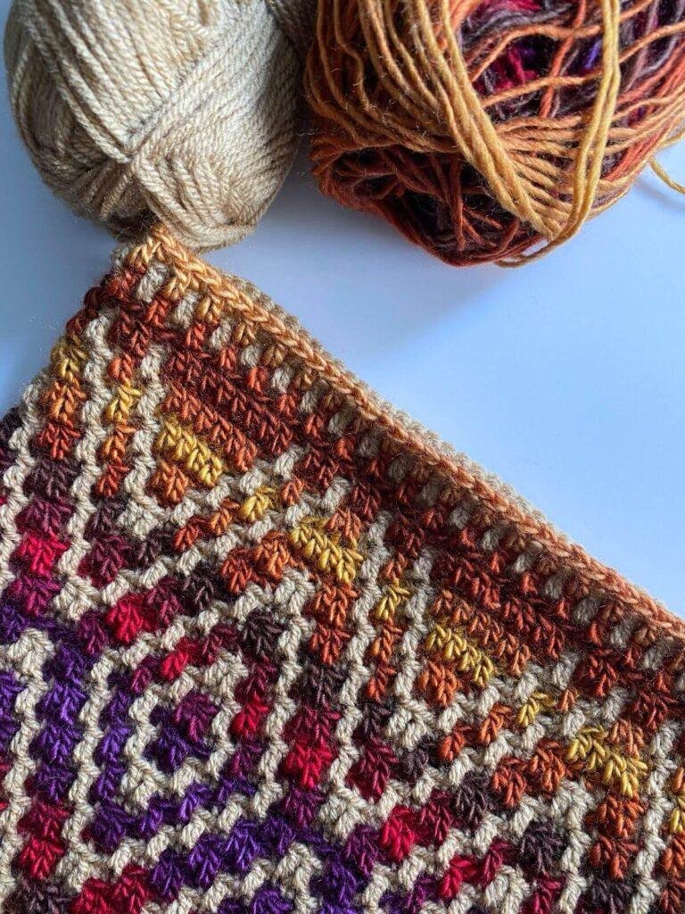 A flatlay of a crochet pillow with diamonds on and the yarn used to make it