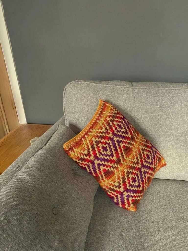 A bright, geometric crochet cushion sits on a great sofa next to a wooden table